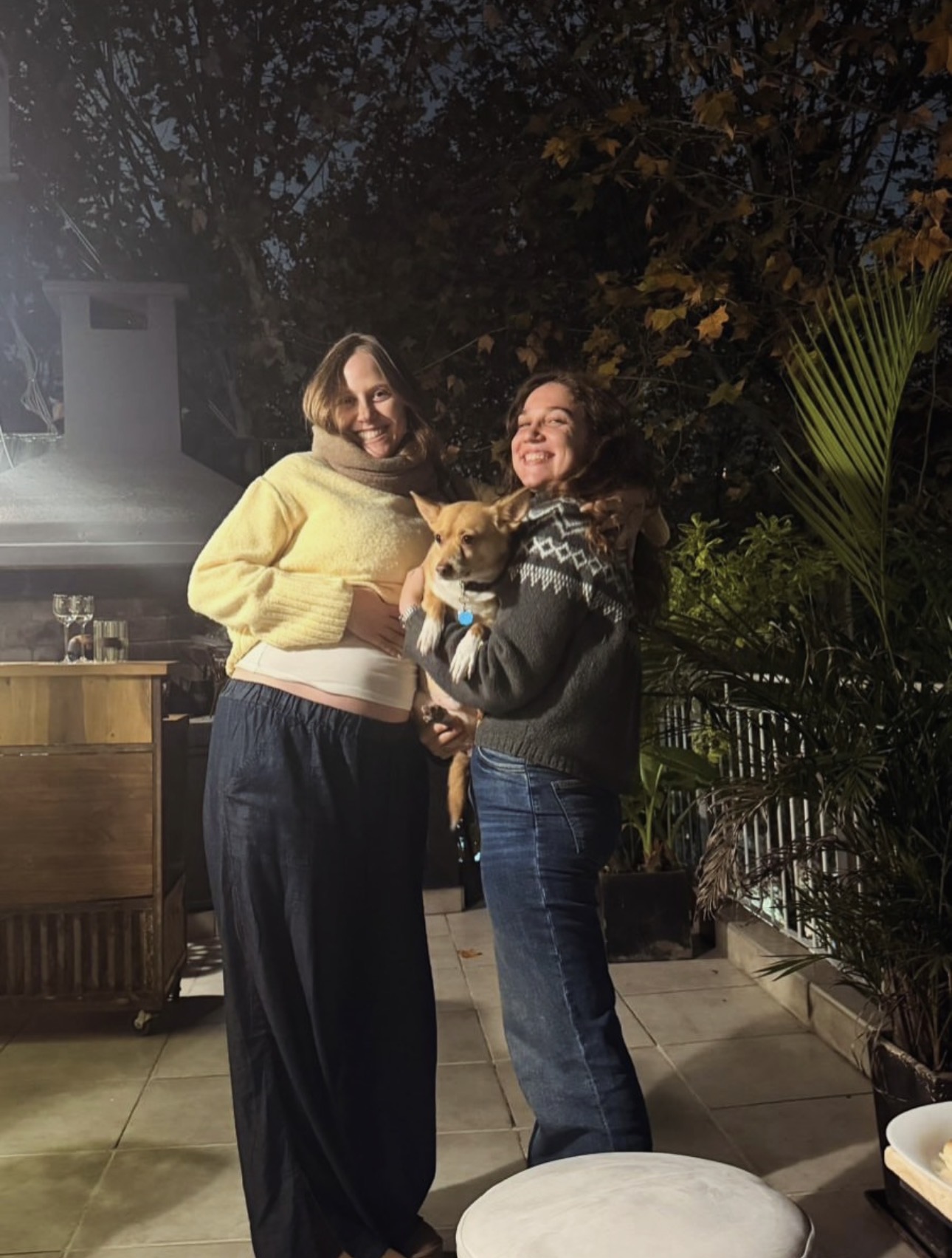 Two guests holding a small dog outdoors at night